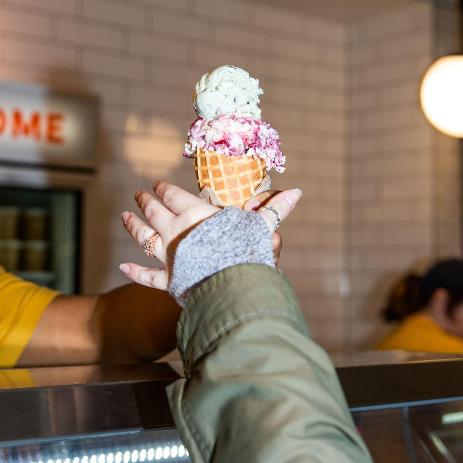 Person handing ice cream cone with three scoops over a counter.
