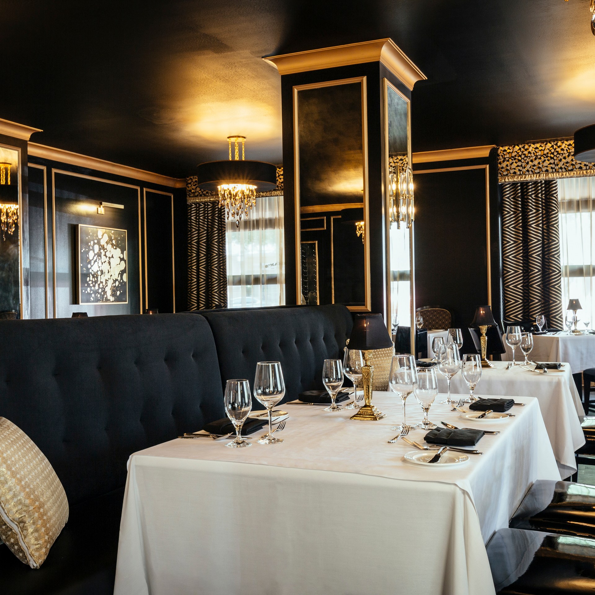 Elegant restaurant with black and gold decor, white tablecloths, and chandelier lighting.