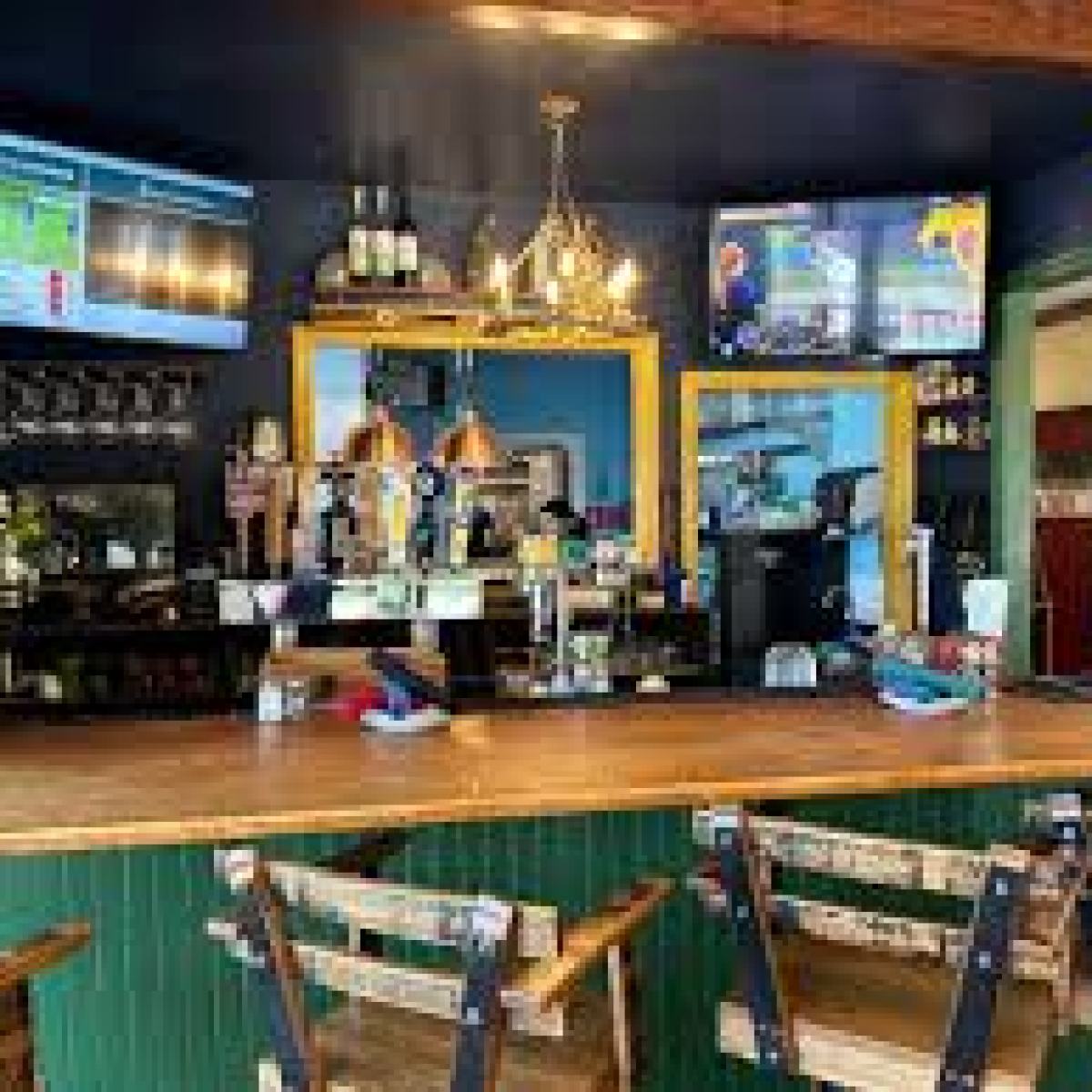 Cozy bar interior with wooden counter, chairs, TVs, and a flower arrangement.