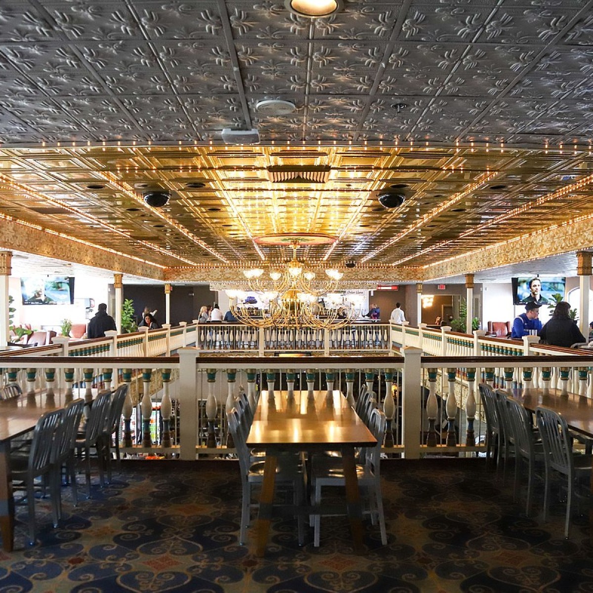 Spacious restaurant with ornate ceiling, wooden tables, metallic chairs, and ambient lighting.