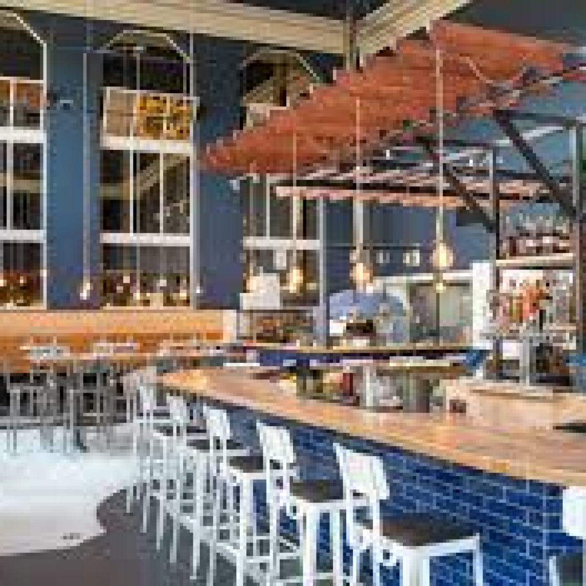 Modern bar with wooden countertops, high stools, and pendant lights in an industrial-style space.