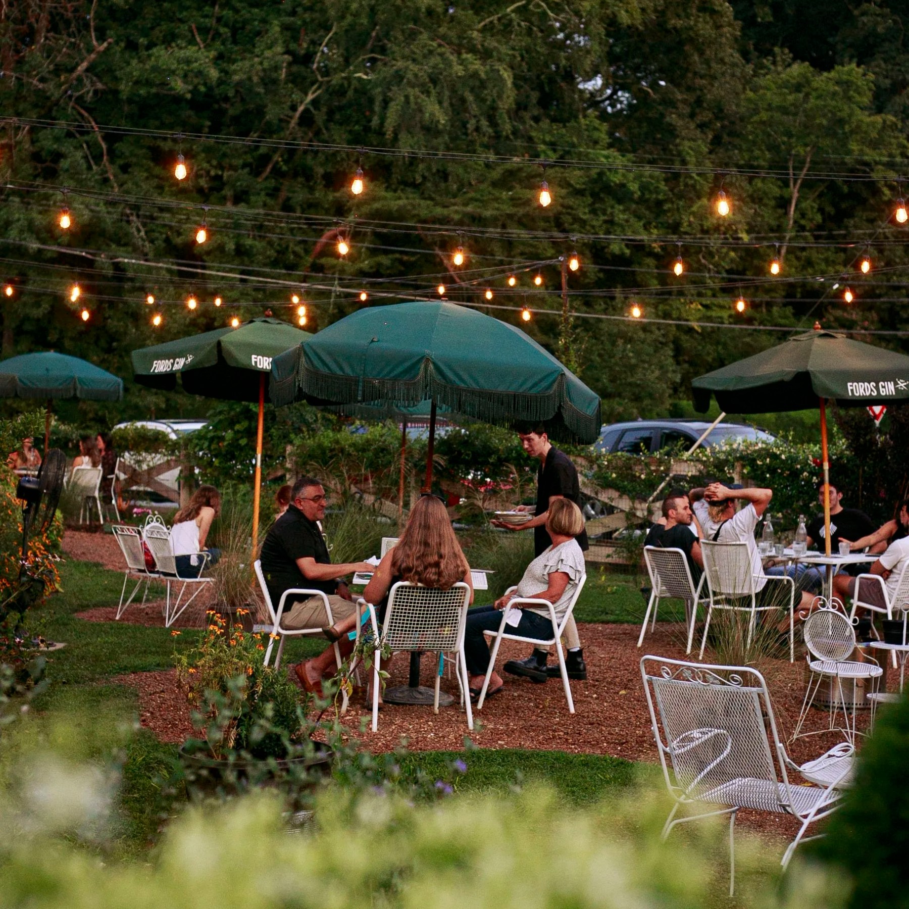 People at outdoor cafe with string lights and green umbrellas.