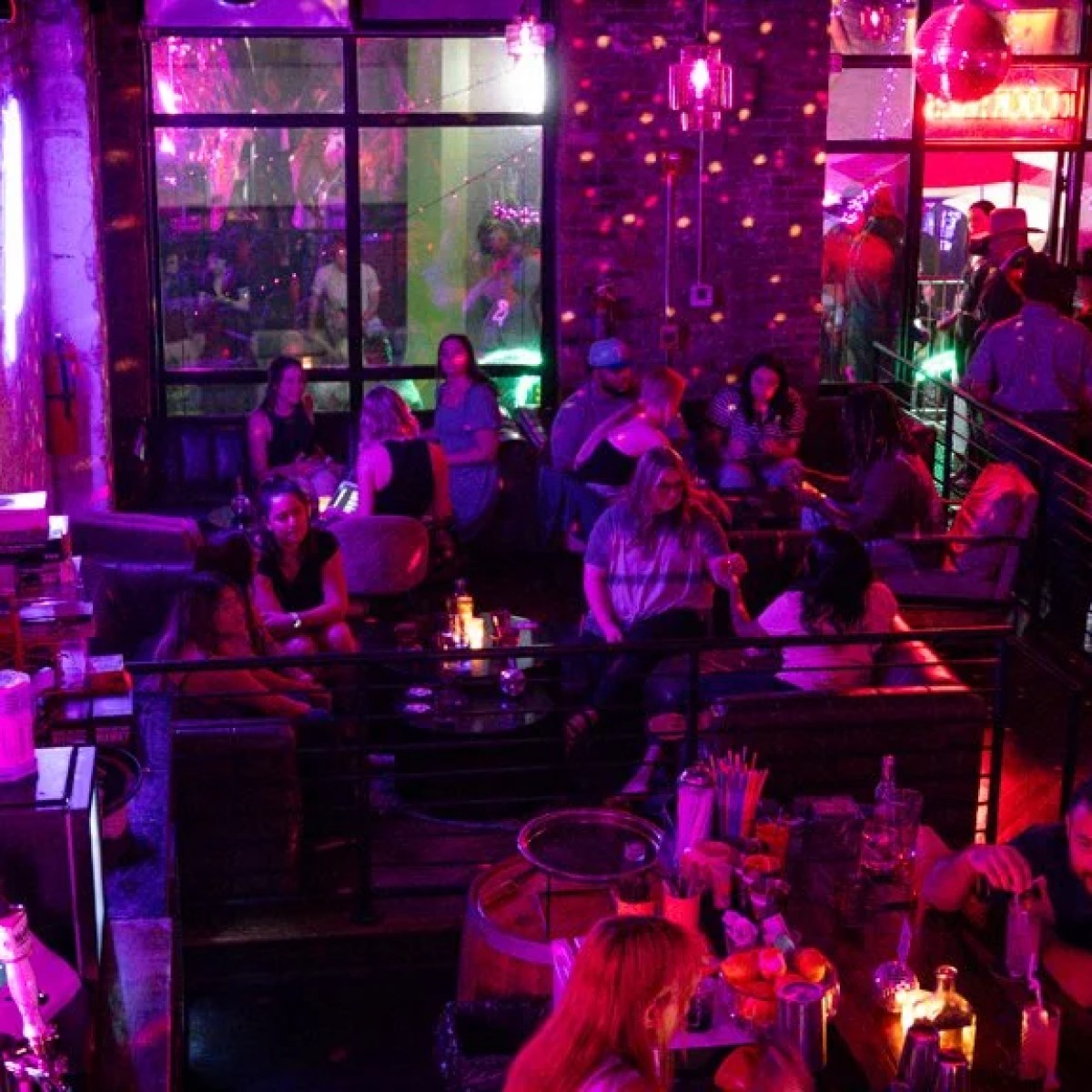 Dimly lit bar with people socializing and colorful lights.