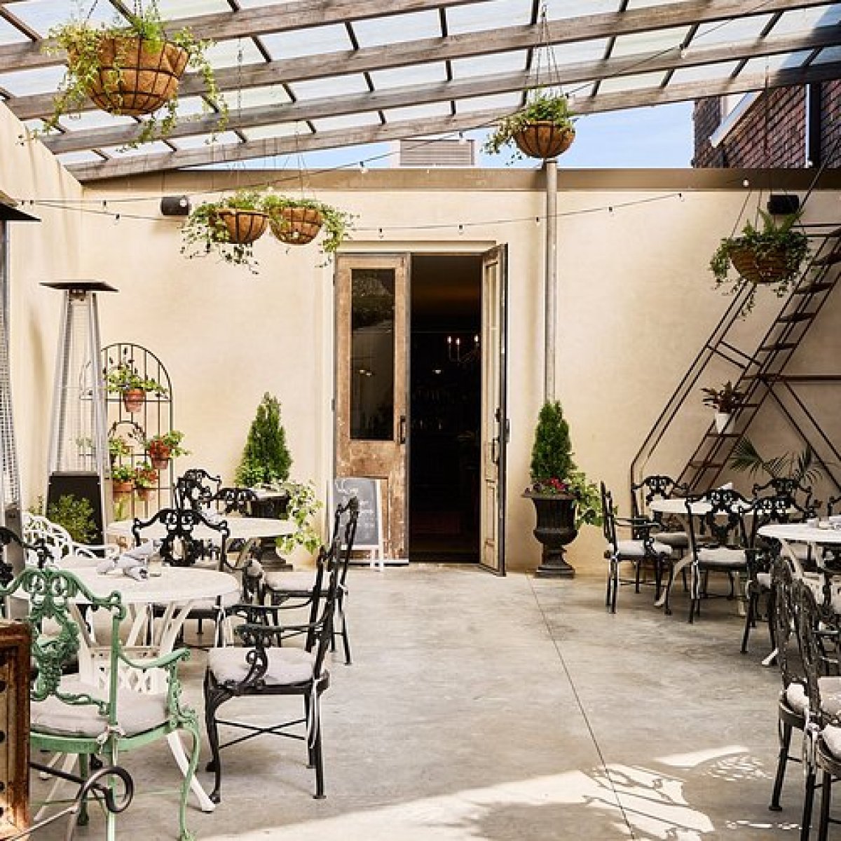 Outdoor patio with tables, chairs, and hanging plants under a glass canopy.