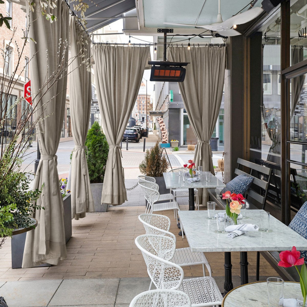 Outdoor cafe seating with white chairs, draped curtains, and small tables with flowers.
